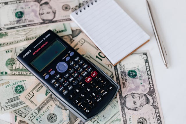 A calculator and notepad sitting on top of some American dollar bills.